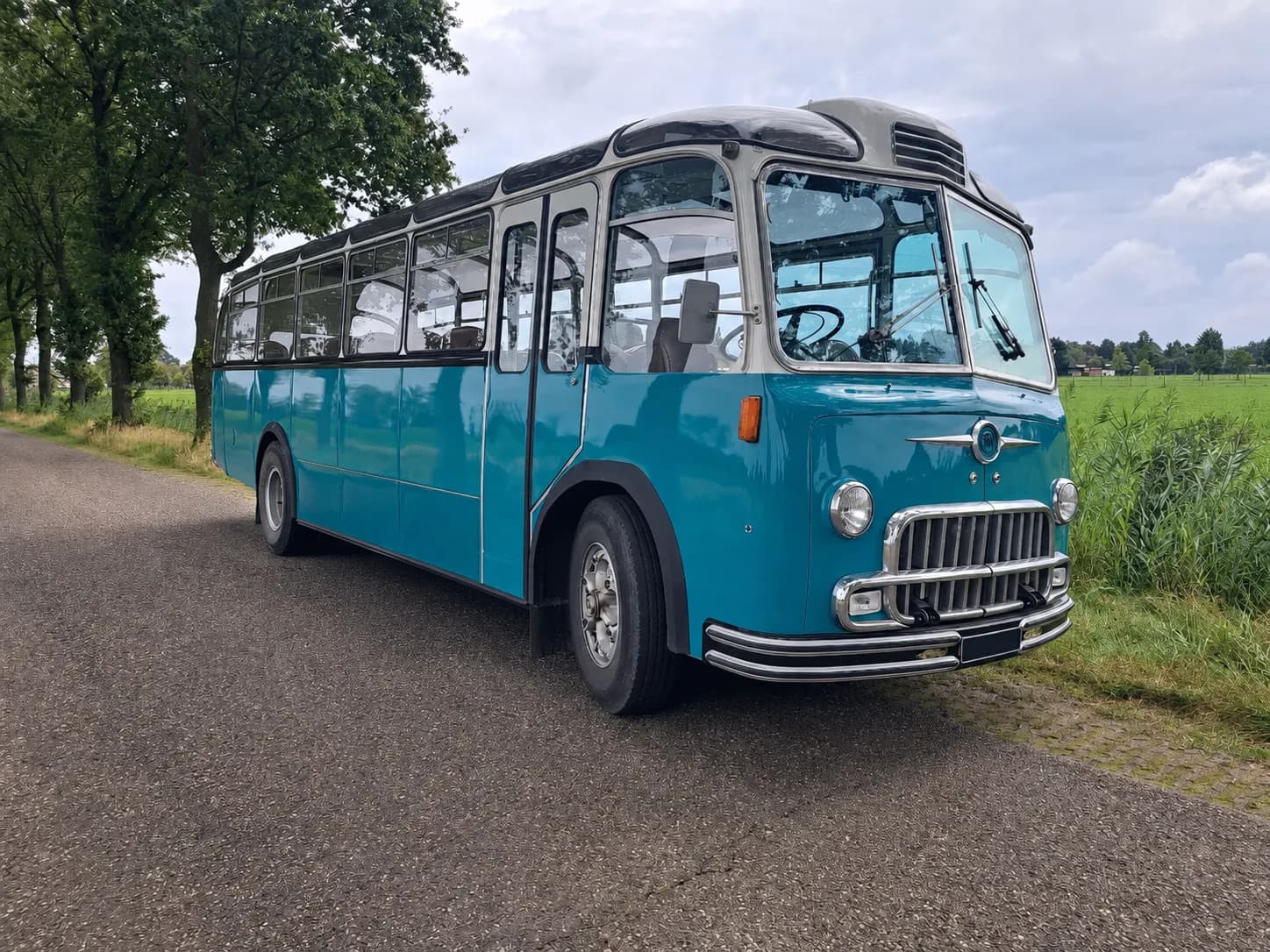 The turquoise Montessori School Bus on a country road between green fields